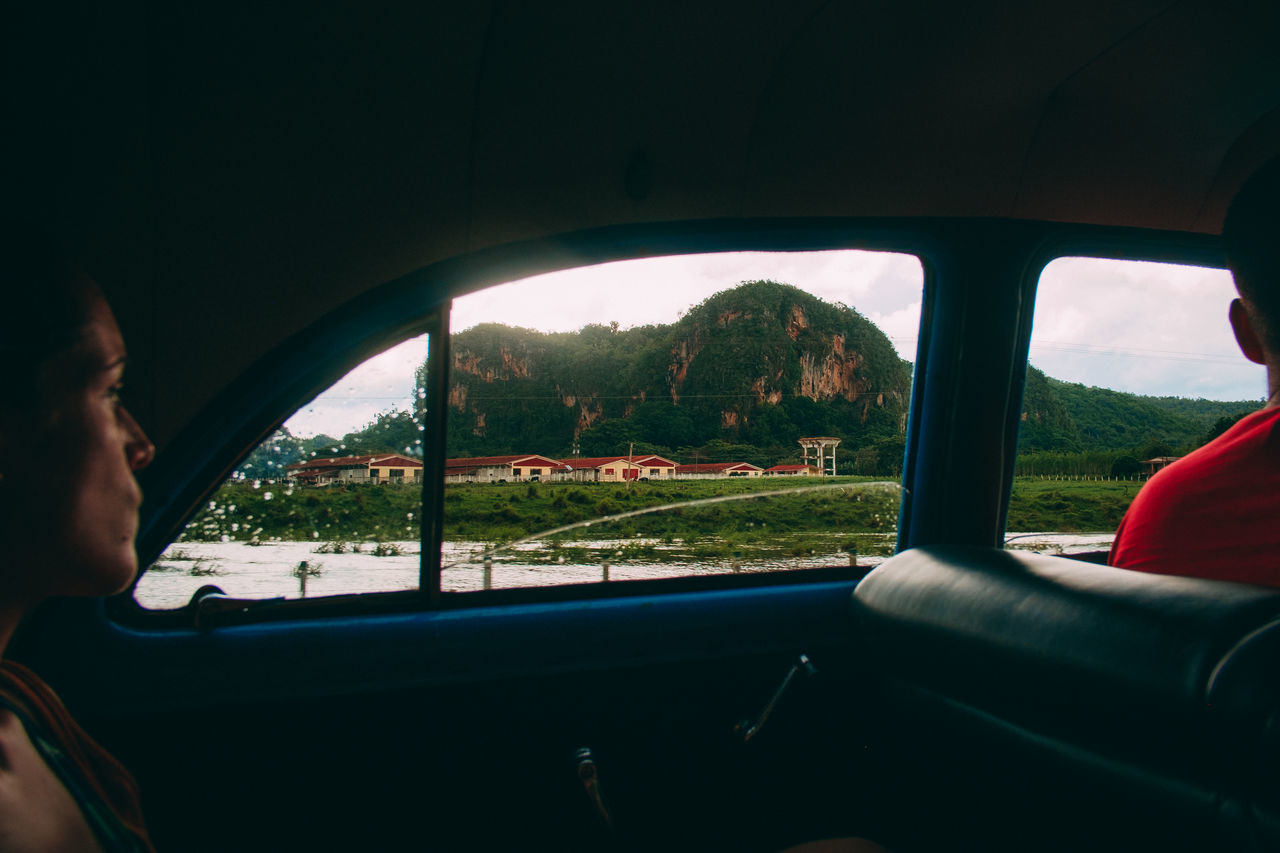 mode of transportation, vehicle interior, car, glass - material, transportation, motor vehicle, transparent, window, land vehicle, men, indoors, real people, lifestyles, day, nature, car interior, sky, travel, leisure activity, two people, hand