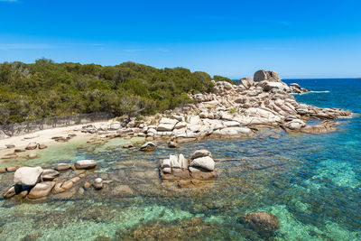 Rocks on shore by sea against blue sky