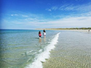 Rear view of friends walking in sea against blue sky