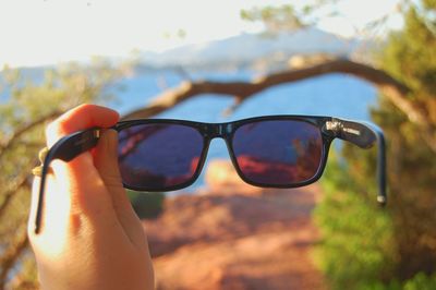 Close-up of hand wearing sunglasses against sky