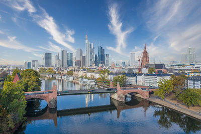 Bridge over river by buildings against sky in city