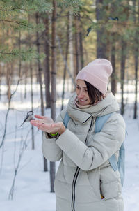 Russian girl in winter in warm clothes in the forest feeds birds with hands