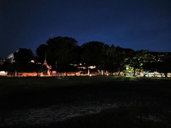 Silhouette trees by illuminated building against sky at night