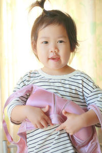 Portrait of girl holding bra while standing against curtain