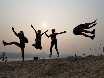 People jumping on beach against sky during sunset