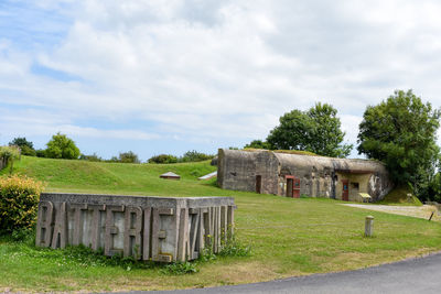 Old house on field by trees against sky