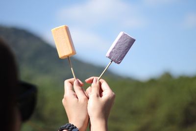 Close-up of hand holding popsicles against sky