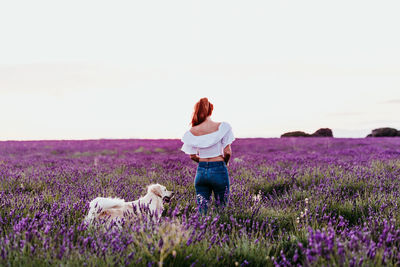 Rear view of woman standing with dog on field against sky