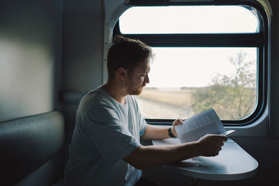 A man is reading a book while traveling by railway train