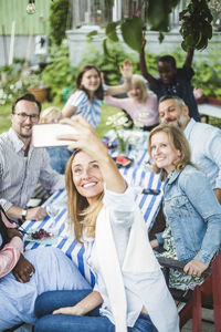 Woman taking selfie with family and friends at dining table in garden party