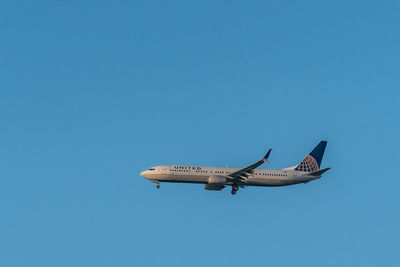 Low angle view of airplane flying against clear blue sky