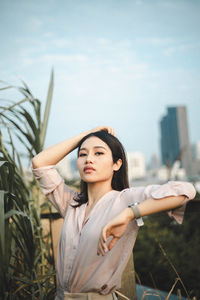 Young woman looking away while standing against plants