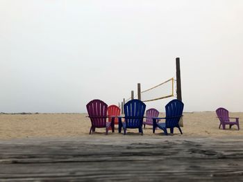 Colorful empty chairs at beach against sky