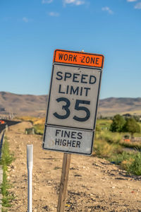 Information sign on road by field against sky