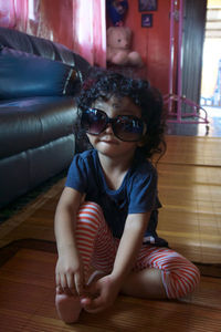 Full length of girl wearing oversized sunglasses while sitting on wooden floor at home