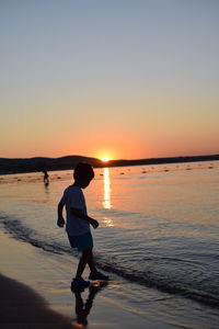 Full length of boy on beach against sky during sunset