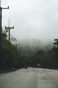 Road by trees against sky during foggy weather