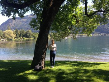 Rear view of woman standing by tree against lake