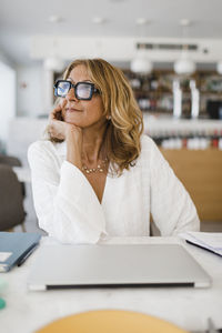 Thoughtful businesswoman with hand on chin sitting at table