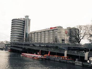 Bridge over river by buildings in city against clear sky