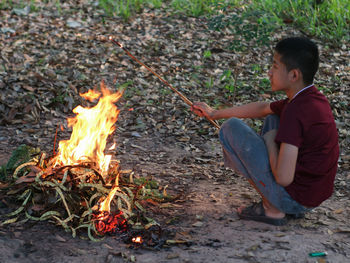 Side view of boy sitting by bonfire