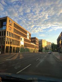 City street by buildings against sky during sunset