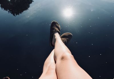 High angle view of woman legs over calm lake during sunny day