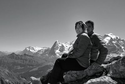 Couple sitting on mountain against clear sky