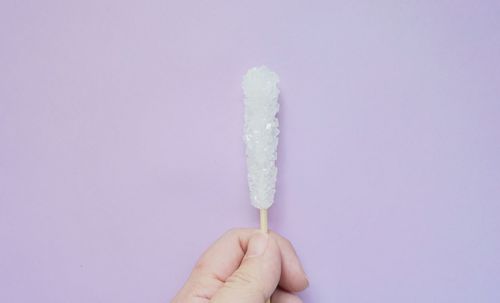 Close-up of hand holding sugar stick against purple background