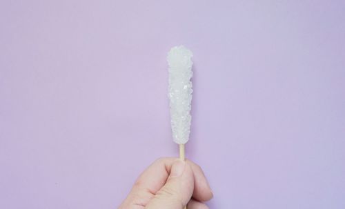 Close-up of hand holding ice cream against white background