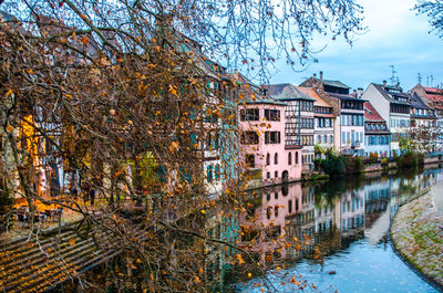 Buildings by river against sky during autumn