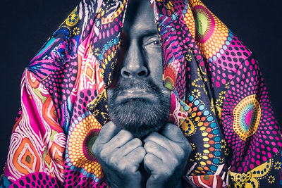 Portrait of man wearing multi colored umbrellas against black background