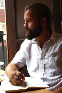 Bearded man with book looking through window in cafe