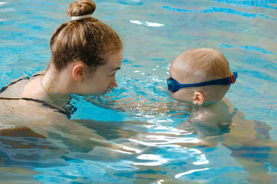 Toddler child learning to swim in indoor swimming pool with teacher. floating in the water