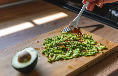 Close-up of person preparing mashed avocado on wooden cutting board