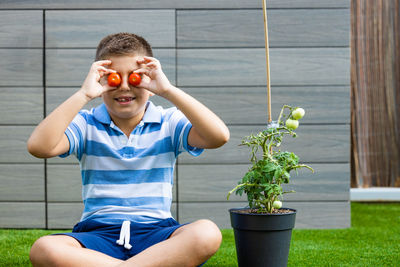 Boy putting tomatoes on his eyes that he has picked from a tomato plant