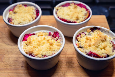 Plums under the crumble in small white bowls placed on a wooden chopping board