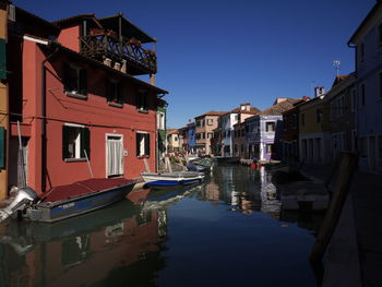 Boats moored in canal amidst buildings against sky