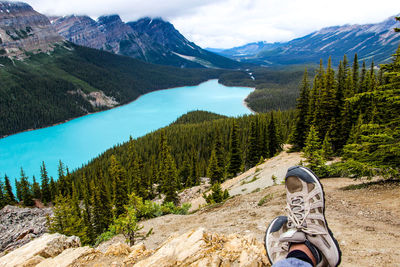 Low section of man over mountain by lake against cloudy sky