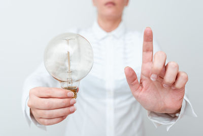 Close-up of hand holding light bulb over white background