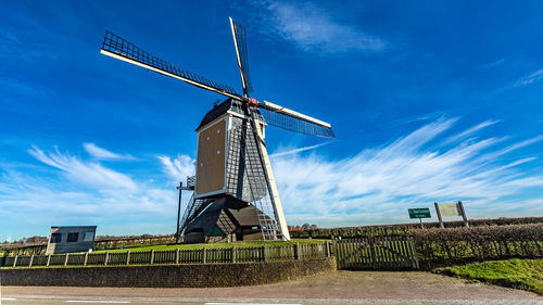 Traditional dutch windmill on field against blue sky, surrounded by a wood fence and farmland