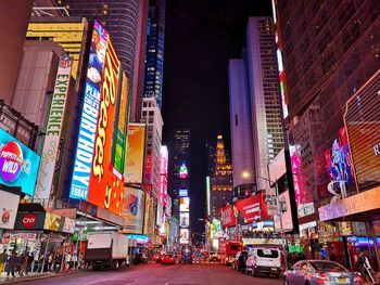 Illuminated street amidst buildings in city at night, new york