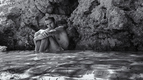 Portrait of depressed young man sitting in sea by rocks