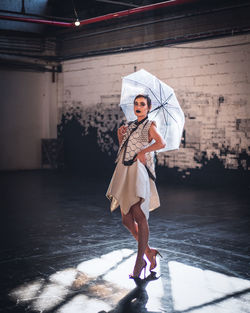 Full length portrait of woman holding umbrella while standing on floor