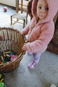 Full length portrait of cute baby girl holding basket with toys at home