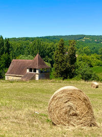 Hay bales on field by house against sky