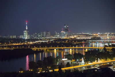 Illuminated buildings by river against sky at night