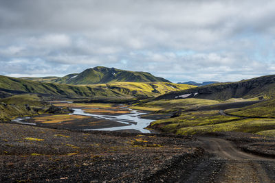 Black dirt road winding through green landscape in iceland