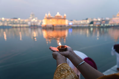 Reflection of hand on water against illuminated river