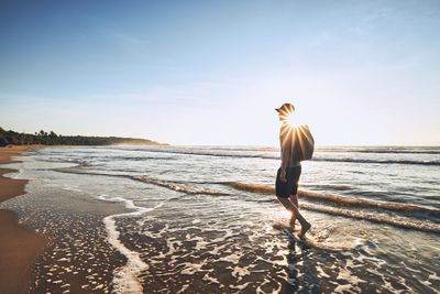 Man walking on beach against sky during sunset